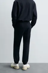 Pantalón jogger negro de corte slim fit, confeccionado en tejido de algodón con cintura elástica ajustable con cordón, bolsillos frontales y traseros de vivo, y bajo con puño elástico.