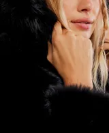 Chaqueta corta de pelo sintético negro con capucha fija y cierre frontal.