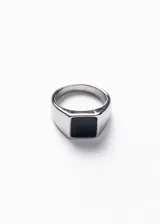 Anillo plateado de acero quirúrgico con piedra negra rectangular en el centro.