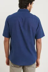 Camisa sport de manga corta color verde oliva, línea premium, con cuello clásico, cierre frontal con botones de coco y bolsillo de parche en el pecho. Confeccionada en lino y algodón.