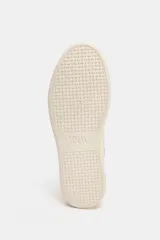 Zapatillas deportivas color beige, con cuerpo en combinación de materiales y cierre mediante cordones. La altura de la suela es de 3 cm.