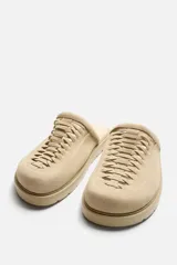 Zueco color beige de piel con acabado serraje, detalle trenzado en el empeine, plantilla acolchada y suela con volumen.