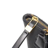 Cartera de mano y hombro color negro, estilo tote bag pequeño, con doble asa corta y correa larga desmontable y regulable. Presenta un bolsillo frontal con solapa y broche dorado, y herrajes metálicos dorados.