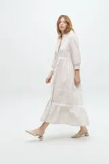 Vestido camisero midi color beige a rayas verticales, con cuello mao, mangas 3/4 abullonadas y festones de algodón en el cuerpo. Cierre frontal con botones.