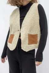 Chaleco marrón de cuero con interior de corderito color crema, cierre con gancho metálico y bolsillos frontales de corderito.