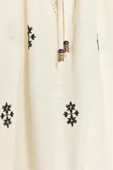 Blusa color crudo de cuello redondo con puntilla, frunces y cordón. Escote pico y manga larga abullonada. Detalle de bordados a contraste en negro.