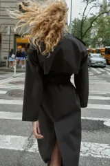 Gabardina larga color beige, con cuello solapa, manga larga con trabillas en hombros y cierre frontal cruzado con botones negros. Incluye cinturón a tono anudado.