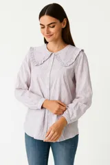 Camisa de algodón a rayas lilas y blancas, con cuello con volados y cierre con botones.