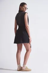 Vestido camisero negro de denim rígido liviano sin mangas, con acceso por botones en delantero y cinto con hebilla metálica plateada.