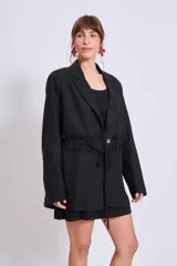 Blazer marrón con solapas de muesca, cierre frontal con lazo y mangas largas. Presenta volados a lo largo de las costuras laterales del pantalón a juego.