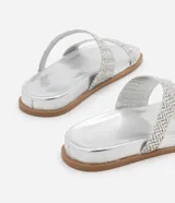 Sandalias planas plateadas con dos tiras trenzadas asimétricas y suela marrón.