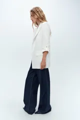 Blazer blanco con cuello solapa y hombreras. Manga por debajo del codo acabada en vuelta con trabilla y botón dorado. Bolsillos delanteros con solapa.