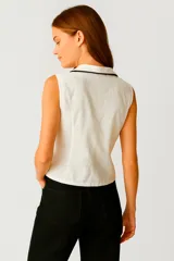 Camisa blanca sin mangas, con cuello clásico, corte al cuerpo y vivos negros en cuello y botones.