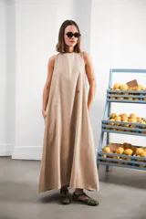 Vestido largo color beige, de corte amplio, con escote redondo, espalda con abertura, bolsillos laterales y logo bordado en el frente.