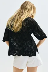Camisa negra de manga corta en punto pointelle suave, con cuello y botones adelante. Ribete festoneado en mangas y bajo.