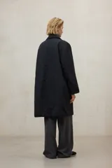 Chaqueta larga de color blanco roto, con cuello camisero y cierre frontal de broches. Presenta un corte holgado y bolsillos laterales.