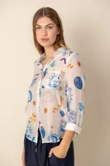 Camisa celeste con estampado de soles, lunas, flores y tortugas en tonos verdes, amarillos y naranjas.