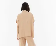 Camisa color beige de corte amplio confeccionada en fibrana, con cuello clásico, manga corta y cierre frontal con botones negros.