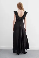 Vestido largo negro sin mangas, con escote redondo, espalda baja y volados en el escote. Ajuste en la cintura con cordón y terminaciones metálicas.
