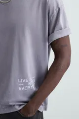 Camiseta gris de corte holgado, cuello redondo y manga corta. Estampado con la frase "Live in Style Everyday" en el frente.