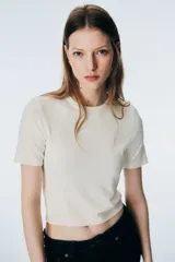 Remera de punto fino color blanco, de manga corta y cuello redondo, con terminaciones acanaladas en puños y bajo.