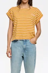 Remera de algodón color mostaza con rayas horizontales finas color rosa pálido. Tiene mangas cortas con dobladillo y un pequeño bordado en el pecho.