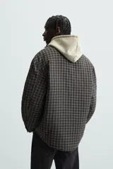 Sobrecamisa de hombre con corte relaxed fit, confeccionada en tejido de algodón acolchado con estampado a cuadros en tonos marrón, negro y beige. Tiene cuello solapa, manga larga con puños abotonados, bolsillo tipo parche en el pecho, aberturas laterales en el bajo y cierre frontal con botones a presión.