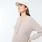 Vestido corto color beige, tipo sweater, de tejido de punto con cuello redondo y manga larga. Presenta una abertura frontal con botones para facilitar la lactancia.