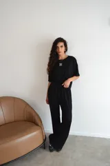 Conjunto de dos piezas color crema, compuesto por una remera de mangas cortas con logo bordado en el pecho y un pantalón palazzo con cintura elastizada y cordón ajustable.