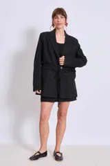 Blazer negro con solapas de muesca, corte holgado, cierre frontal con lazo y detalle de volados en los bolsillos.