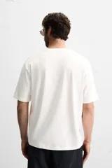 Camiseta blanca de corte holgado, cuello redondo y mangas cortas. Presenta un bordado y estampado combinado en el frente.