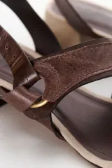 Sandalia de mujer color beige claro con taco bajo y grueso de color negro. Presenta tiras cruzadas en el empeine con un detalle de argolla metálica y tira de ajuste con hebilla en el talón.