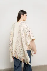 Ruana de tejido crochet color crudo con detalles de hilos de colores y flecos en el borde inferior.