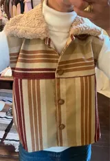 Chaleco con estampado a rayas verticales en tonos beige, marrón y rojo, con cuello de piel sintética color crema y cierre frontal con botones.