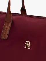Cartera tote de nailon color borgoña, con forma flexible y asas superiores de cuero marrón. Presenta un cierre de cremallera, bolsillo interior con cremallera y dos bolsillos abiertos interiores. En el frente lleva una insignia metálica dorada con el monograma TH.