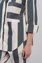 Camisa con corte estilo blazer, a rayas verticales color gris y blanco, con cuello clásico, cierre frontal con botones, bolsillo de parche en el pecho y mangas largas amplias.