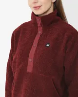 Buzo polar gris de mujer con cuello alto abotonado y bolsillo tipo canguro. Tiene un parche redondo con el logo de Cat en el lado izquierdo del pecho y broches con el logo de Cat en la parte delantera.