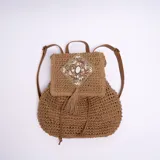 Mochila marrón tejida con detalles de piedras y lentejuelas en la solapa. Tiene correas ajustables de cuero sintético y cierre con cordón ajustable.