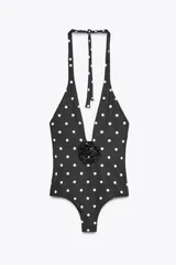 Bañador negro con estampado de lunares blancos, copas extraíbles, cuello halter con lazada y escote pico pronunciado. Detalle de flor en relieve en el pecho.