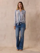 Blusa de gasa estampada a rayas verticales en tonos celeste, lila, naranja y marrón. Tiene cuello a la base con escote en V y botones. Delantera con bolsillo aplicado. Largo de manga regulable con presilla y botón. Terminación anudada opcional.
