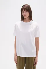 Remera blanca de algodón, de manga corta y cuello redondo. Presenta un detalle bordado y calado en el hombro derecho con motivos florales.