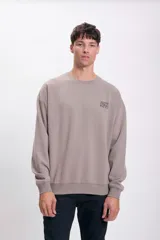 Buzo deportivo color gris topo, de corte holgado y manga larga. Presenta un pequeño estampado en el pecho.