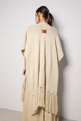 Ruana color beige de tejido de punto con flecos en el ruedo.