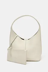 Bolso formato saca color crudo, confeccionado en piel con efecto granulado. Tiene asa de hombro y cierre con imán. Incluye cartera con bolsillo extraíble.