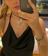 Collar con dije de sol hecho en bronce y cuero sintético, con tiento negro y cierre ajustable.