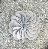 Broche con forma de flor color gris claro, realizado artesanalmente en Italia con pétalos de cuero dispuestos en espiral. Se aplica con imán.