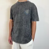 Remera gris con efecto gastado, corte semi oversize y estampado en el pecho con diseño abstracto circular en tonos amarillo, celeste y blanco.