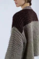 Cárdigan tejido de punto grueso color gris con detalles en verde y marrón. Tiene escote en V profundo, cierre frontal con botones, mangas abullonadas y corte cropped.