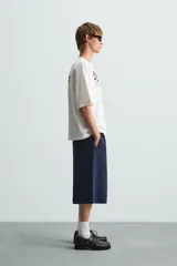 Camiseta blanca de corte holgado, cuello redondo y manga corta. Presenta estampados combinados en negro en la parte delantera y trasera.