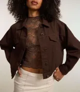 Campera marrón de sarga de algodón, corte regular, cuello inglés, manga larga, abotonada al frente, con bolsillos con solapa en el pecho y pliegues en la parte baja.